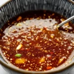 Thick homemade stir fry sauce with sesame seeds and vegetables in a blue striped bowl