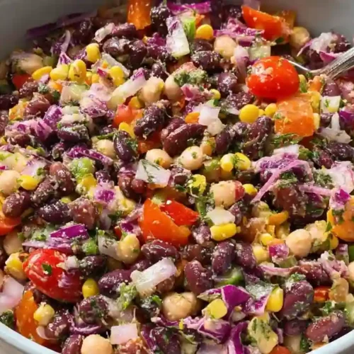Colorful dense bean salad with black beans, chickpeas, corn, cherry tomatoes, and red cabbage in a white bowl