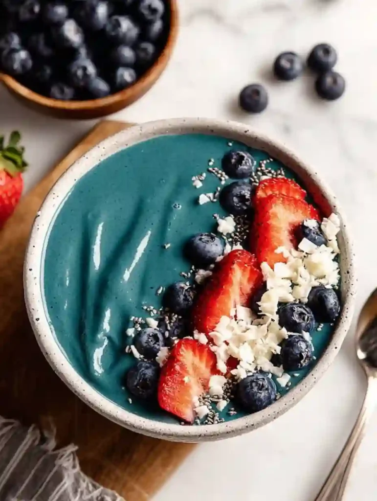 Close-up of blue spirulina smoothie showing strawberry slices blueberries shredded coconut and chia against a creamy teal swirl