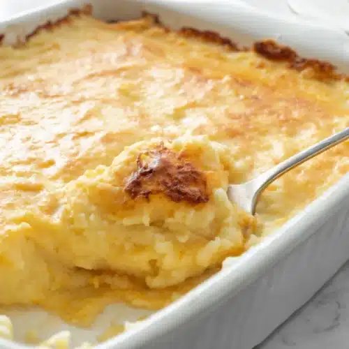 Creamy mashed potato casserole in a white baking dish with a golden top.
