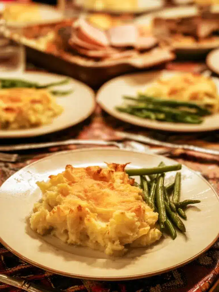 Slices of mashed potato casserole served on plates with turkey and green beans.