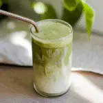 Iced Banana Matcha Latte in a tall glass, with a vibrant green top layer and creamy, mashed banana swirling at the bottom, showcasing the dual texture.