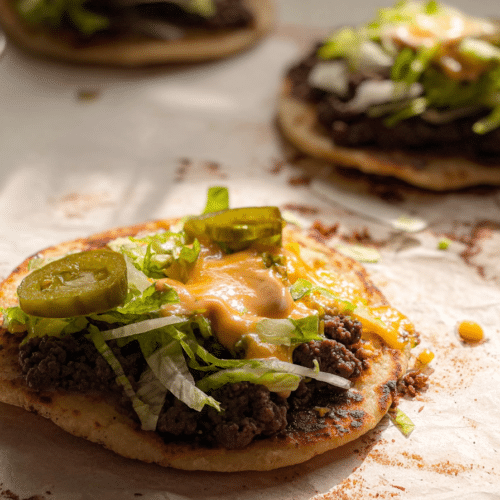 Close-up of a stack of Big Mac Smash Tacos, showing crispy beef patties infused with smoked paprika and Worcestershire sauce, melted cheese, shredded lettuce, and special sauce.