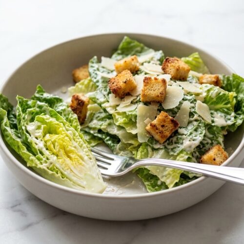 A vibrant caesar salad recipe featuring crisp romaine lettuce, shaved Parmigiano-Reggiano, and golden-brown Umami-Crusted Miso Croutons scattered on top.