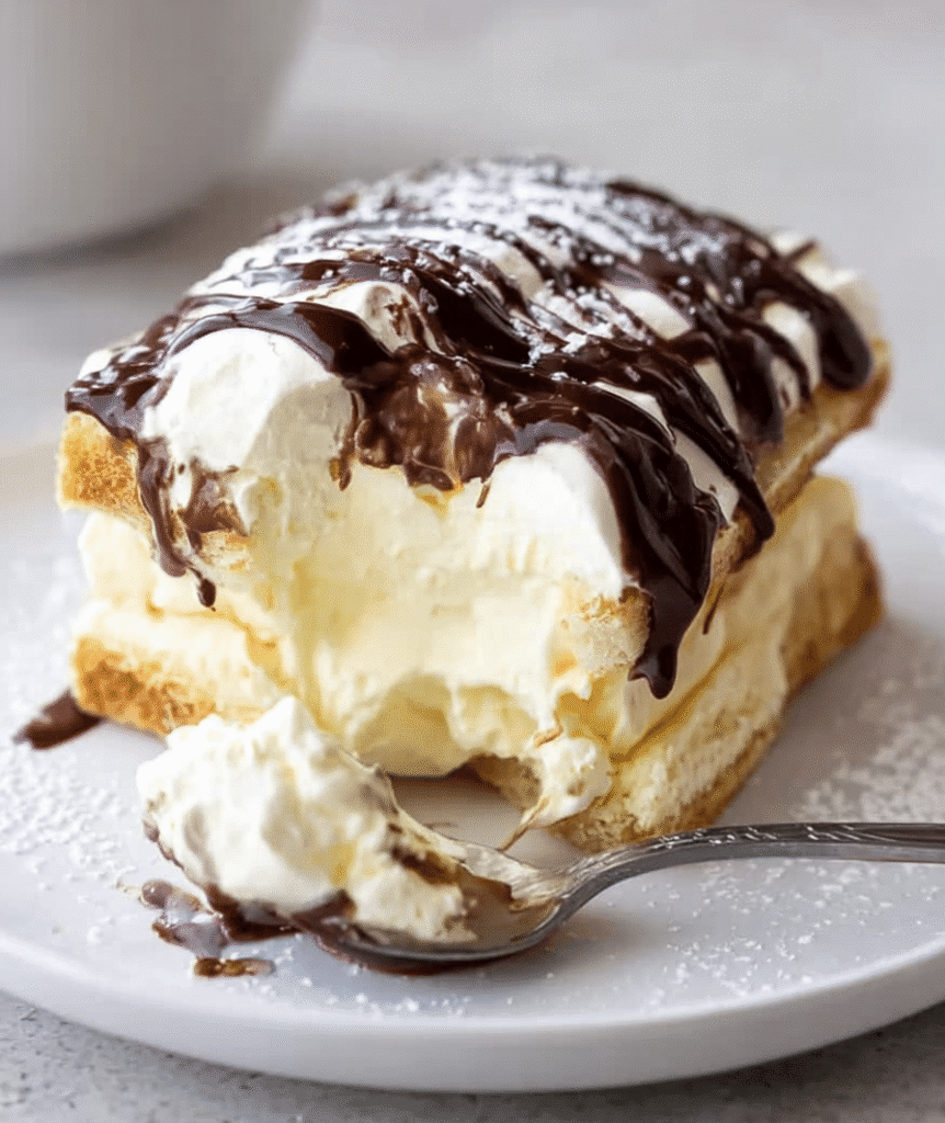 A close-up view of the interior layers of Chocolate Eclair Cake showing the crisp crust, creamy filling, and smooth chocolate ganache.