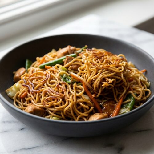 Close-up of golden brown chow mein noodles speckled with vegetables and chicken, showcasing the Double-Sear Noodle Method for extra crispiness.