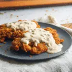 Golden-brown country fried steak with a uniquely craggy, crispy crust thanks to buttermilk powder and cornstarch, topped with creamy white gravy.
