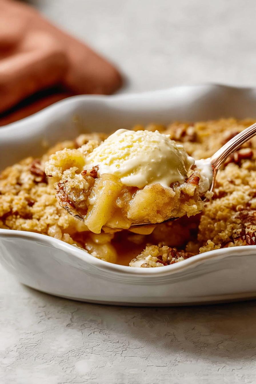 Close-up of a warm slice of apple dump cake recipe, showing the golden, crisp pecan streusel topping and tender, bubbling apple filling.