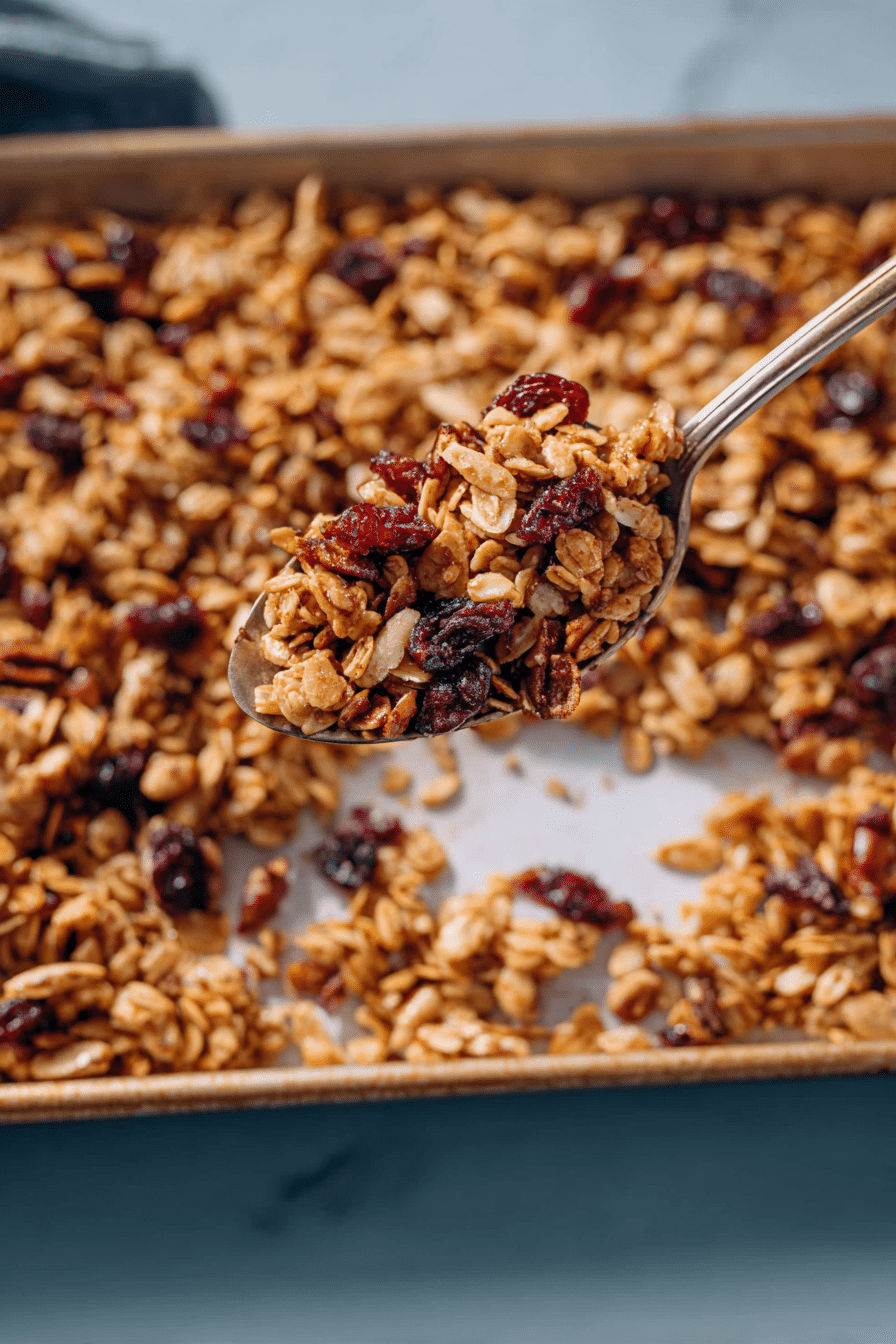 A macro close-up of crunchy granola clusters, showing the toasted oats, nuts, and subtle orange flecks.