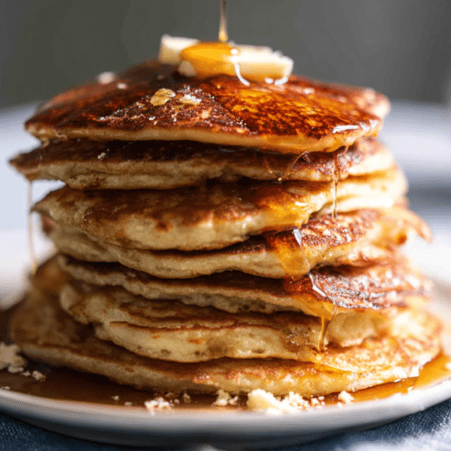 Stack of golden brown double-malt brown butter pancakes drizzled with syrup and topped with a pat of butter, emphasizing the unique pancake mix.