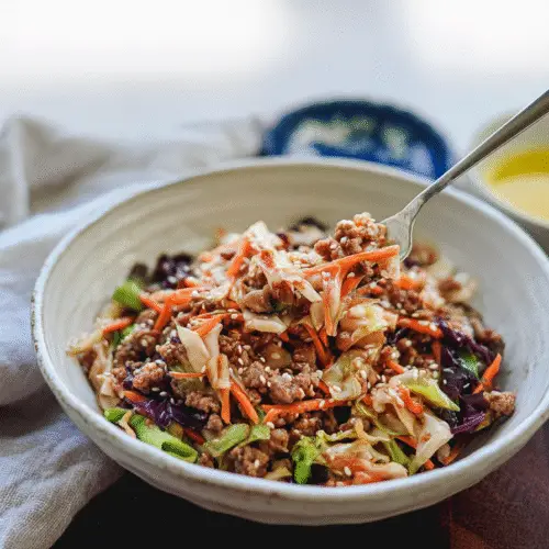 Hearty egg roll in a bowl with savory ground pork and finely chopped shiitake mushrooms, garnished with toasted sesame seeds and a drizzle of sesame oil.
