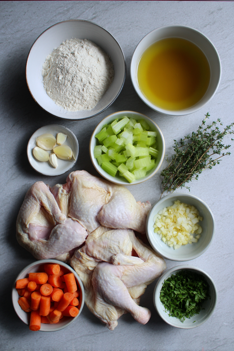 Raw ingredients laid out for a smothered chicken recipe, including chicken thighs, mirepoix, flour, and chicken broth.