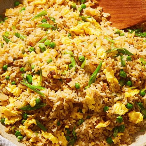 A vibrant bowl of Fried Rice, each grain coated in golden egg, topped with fresh scallions and red chili.