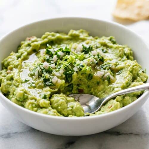 Bright green guacamole recipe in a molcajete, garnished with cilantro and a lime wedge, showcasing the smooth texture from Citrus-Aromatic Maceration.
