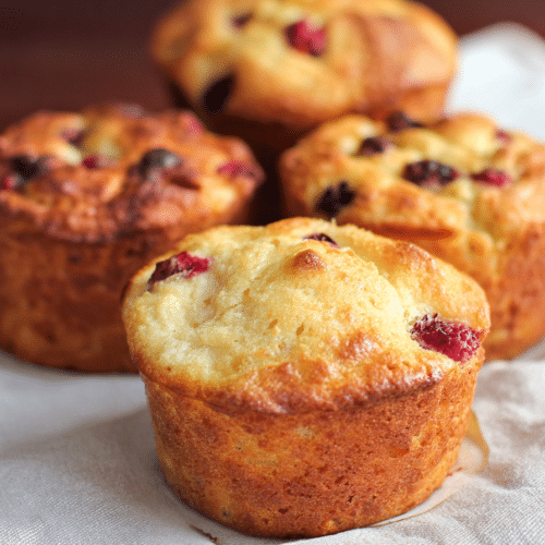 A stack of golden-brown high protein cottage cheese muffins no banana, with fresh berries on top, showing their moist cheesecake-like texture.