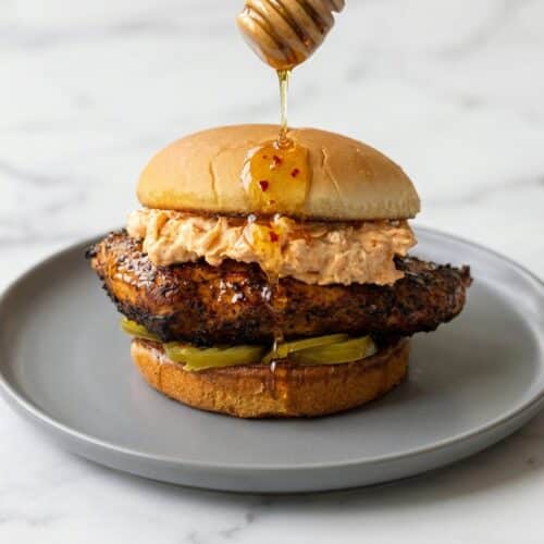 A fried honey pepper pimento chicken sandwich with a golden crispy exterior, featuring a hot honey pickle brine soak and creamy pimento cheese on a potato bun.