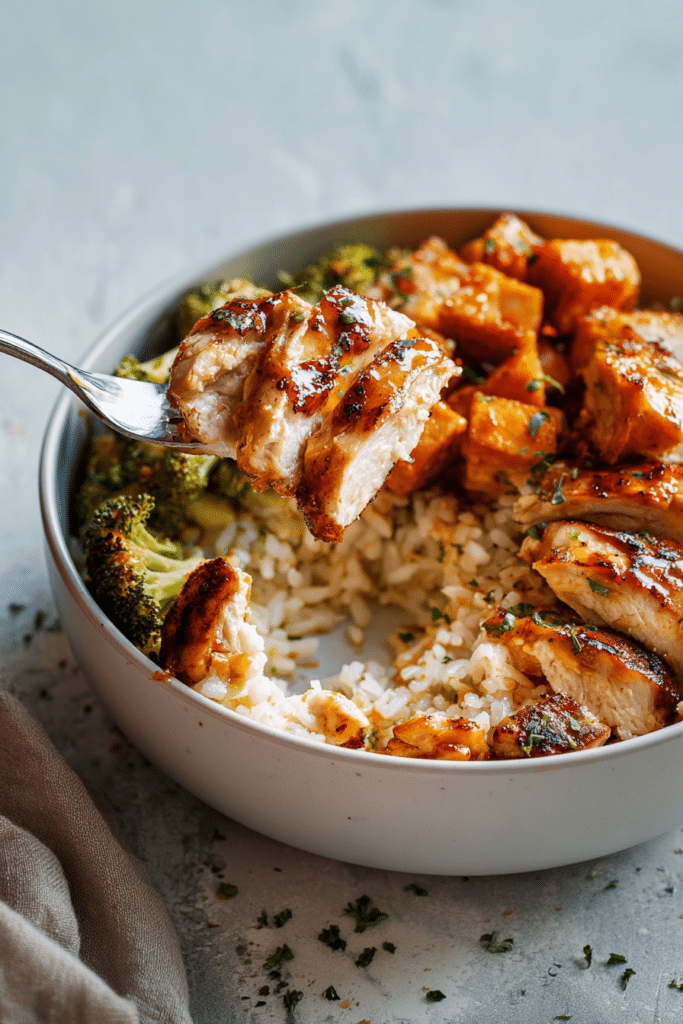 Close-up texture of perfectly roasted hot honey chicken, showing the crispy, caramelized skin and tender meat in a cottage cheese rice bowl.