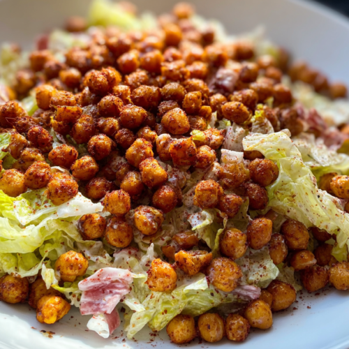 A vibrant iceberg lettuce salad with golden, air-fried crispy chickpeas and a creamy dressing, presented in a large serving bowl.