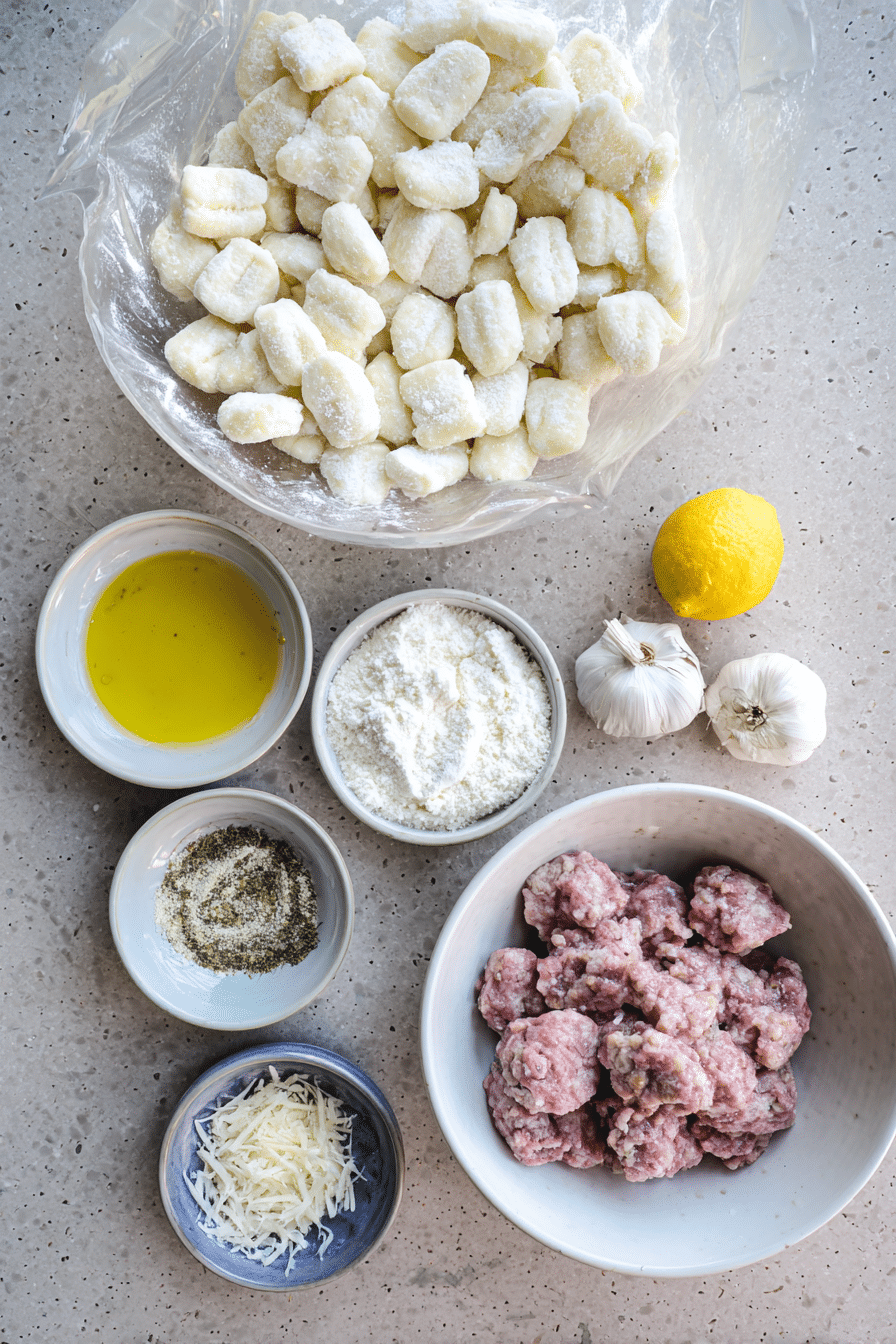 Overhead view of raw potato gnocchi, broccoli florets, Italian sausage, garlic, and dried Calabrian chilies for Crispy Sheet Pan Gnocchi.