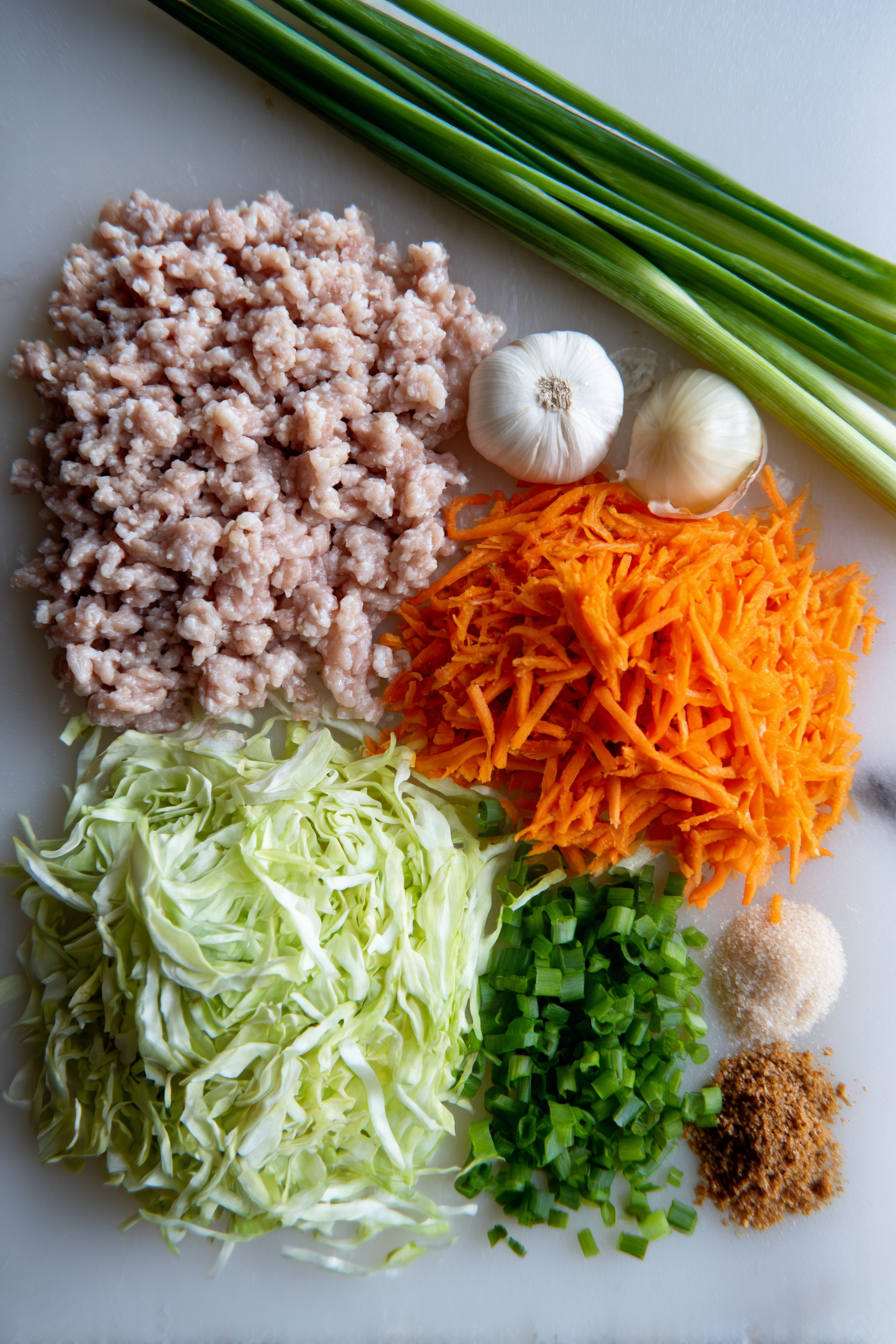 Flat lay of fresh ingredients for egg roll in a bowl, featuring ground pork, shiitake mushrooms, coleslaw mix, soy sauce, and aromatics.
