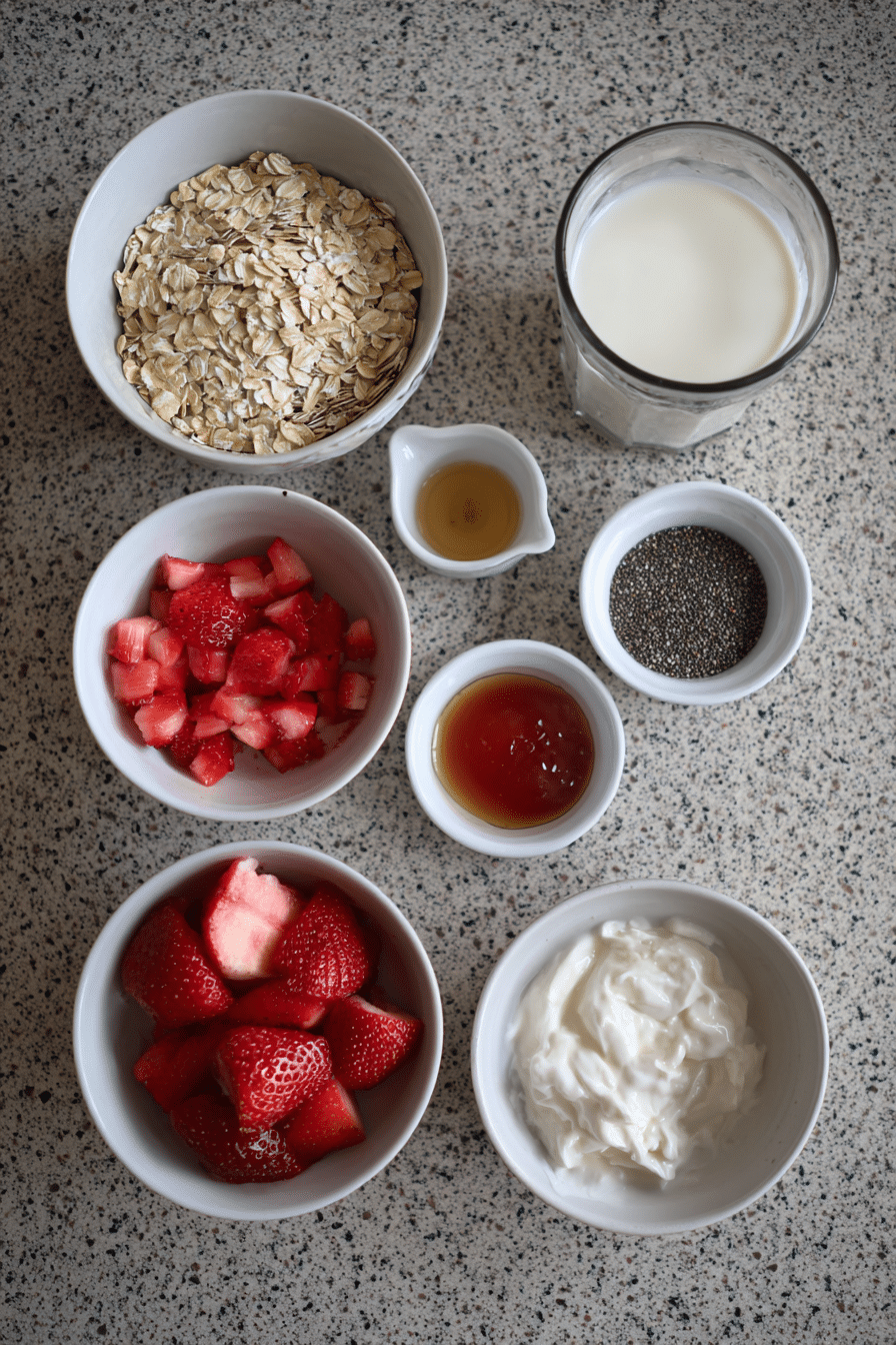 A flat lay of ingredients for strawberry shortcake overnight oats, including rolled oats, fresh strawberries, and shortbread cookies.