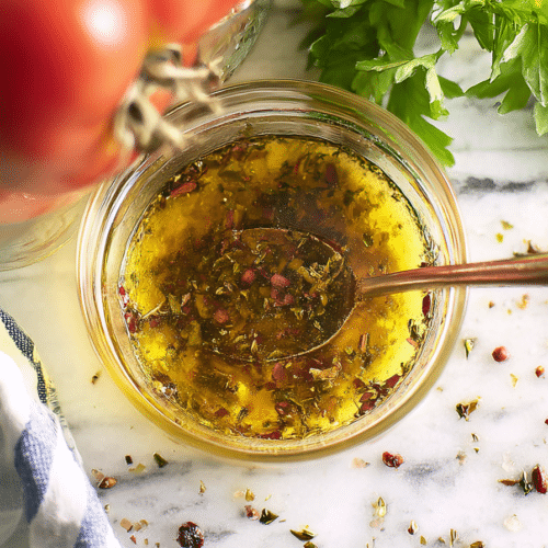 Golden homemade Italian dressing in a glass bottle, showcasing the richness from bloomed dried herbs.