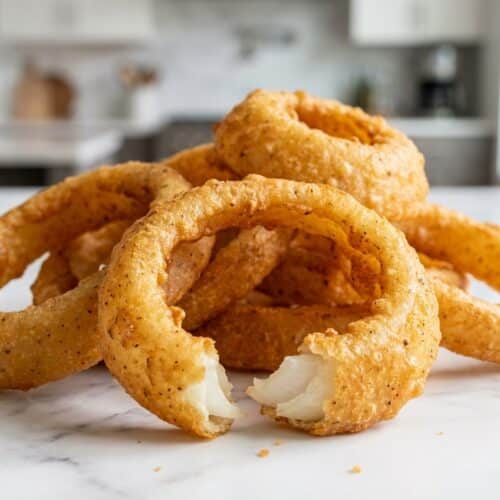 Crispy golden onion rings recipe showing multiple double-dipped rings piled high on a white plate, glinting from the chilled vodka batter.