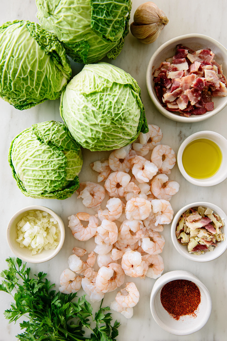 Flat lay of raw ingredients for a cabbage boil with shrimp and sausage, including fresh cabbage, plump shrimp, sliced andouille sausage, and vibrant Cajun seasoning.