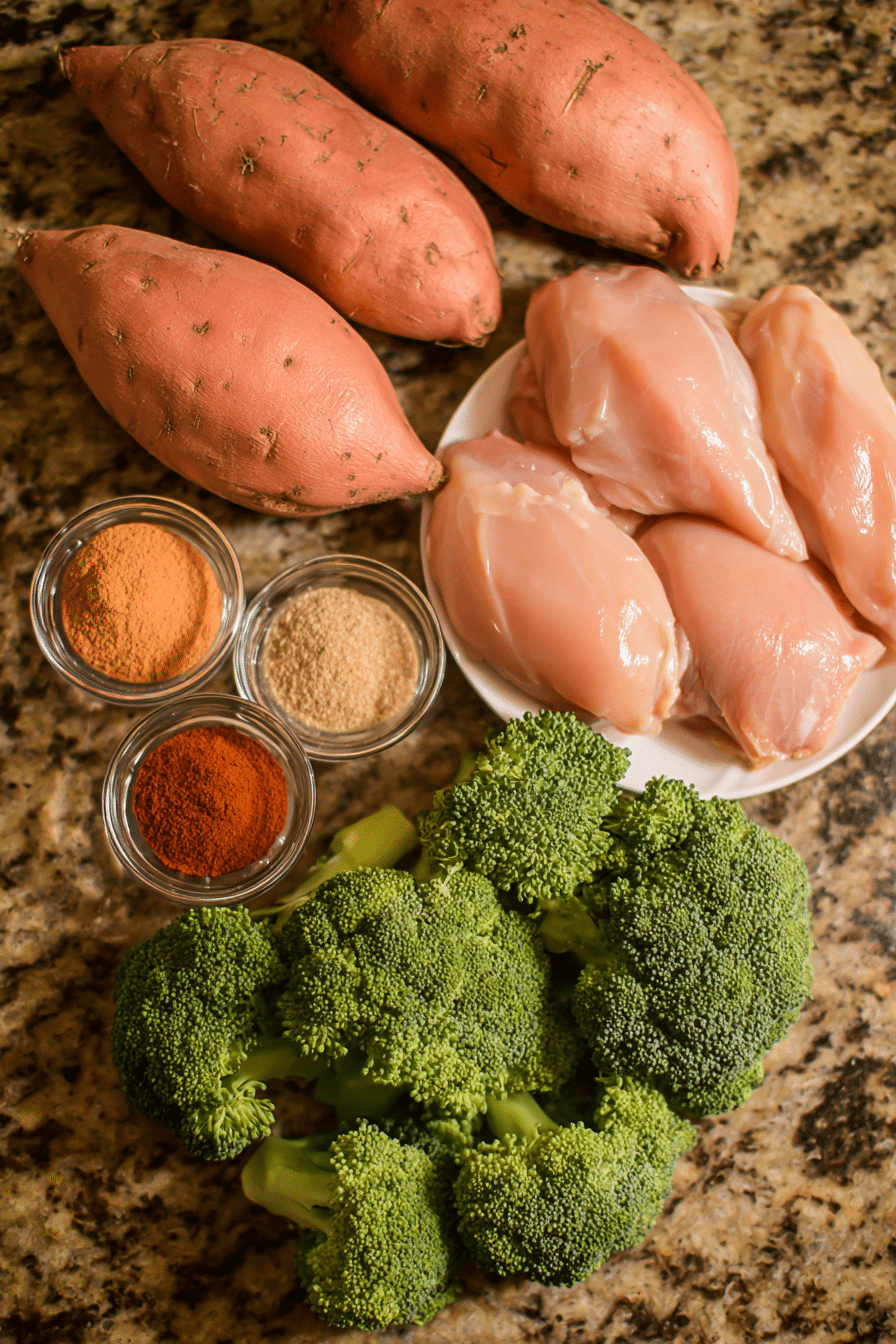A flat lay of raw ingredients for hot honey cottage cheese chicken rice bowl, including boneless skinless chicken thighs, sweet potatoes, and broccoli.