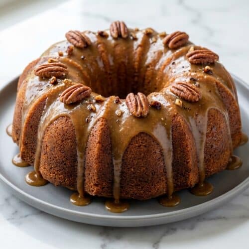 A glistening salted caramel kentucky butter cake, drizzled with rich brown butter sauce, on a white cake stand.