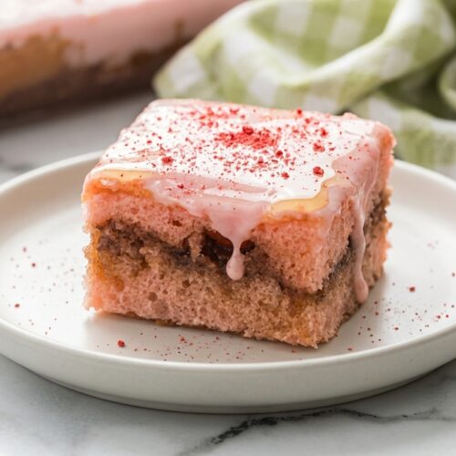 A slice of strawberry honey bun cake topped with a generous real honey infused glaze and bright freeze-dried strawberry dust.