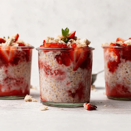 A close-up of fully assembled strawberry shortcake overnight oats in a glass jar, topped with golden, buttery shortcake crumble.