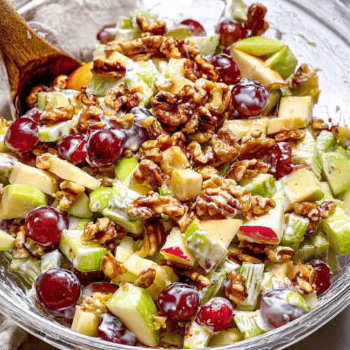 A fresh Waldorf Salad in a clear bowl, with Miso-Maple Glazed Walnuts sprinkled on top, showcasing crisp apples and grapes.
