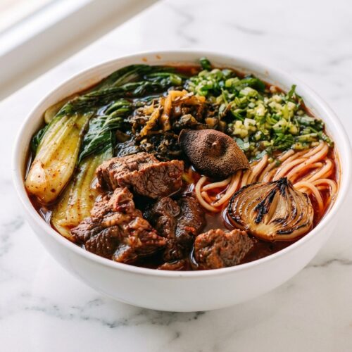 Beef noodle soup with charred onion ginger broth and a hint of fragrant dried tangerine peel in a deep ceramic bowl.