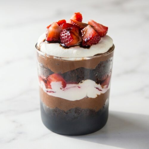 Layered brownie strawberry trifle with espresso-balsamic macerated berries and whipped cream in a glass bowl.