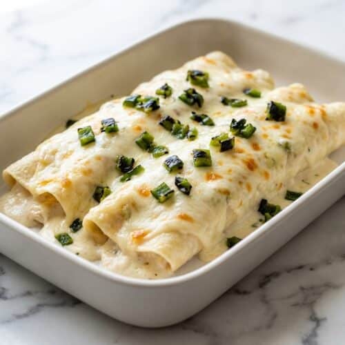 Bubbling creamy white chicken enchiladas with fire-roasted poblanos and melted Monterey Jack cheese in a baking dish.