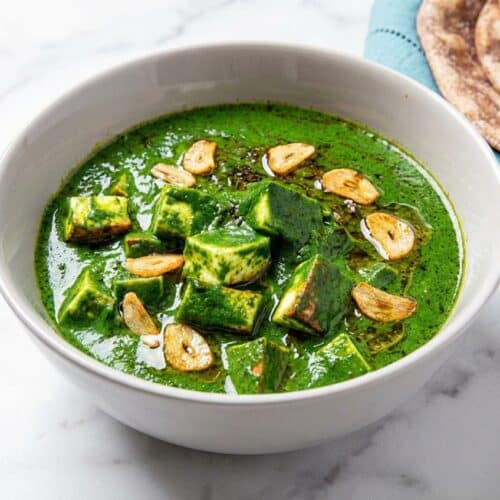 Creamy palak paneer recipe topped with a golden, sizzling double-garlic tadka finish in a rustic bowl.