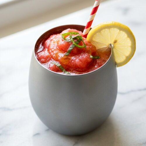 Frozen strawberry lemonade in a tall glass, elevated with a fragrant honey-basil maceration and fresh garnish.