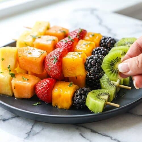 Vibrant fruit kabobs drizzled with a glossy honey-lime-mint finishing glaze on a serving platter.