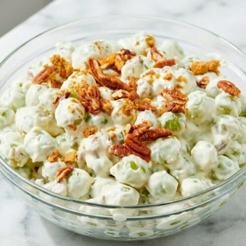 Creamy grape salad topped with crunchy salted cinnamon-toffee pecans in a white serving bowl.