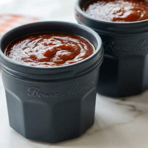 Glossy, dark homemade bbq sauce recipe with a rich bourbon-maple reduction in a glass jar.