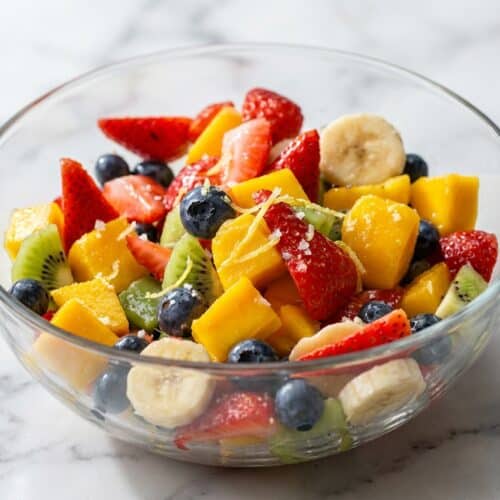 Honey Lime Rainbow Fruit Salad in a bowl, glazed with ginger-infused dressing and a pinch of sea salt.
