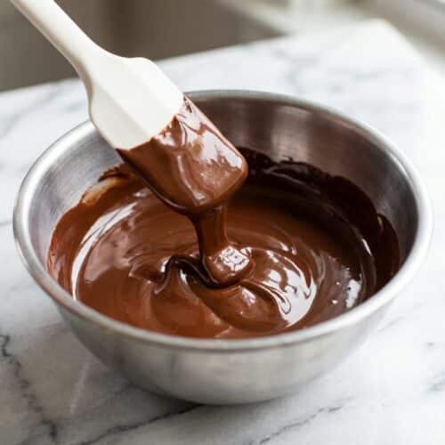 Glossy liquid chocolate swirling in a bowl showing how to melt chocolate using the silky sheen oil hack.