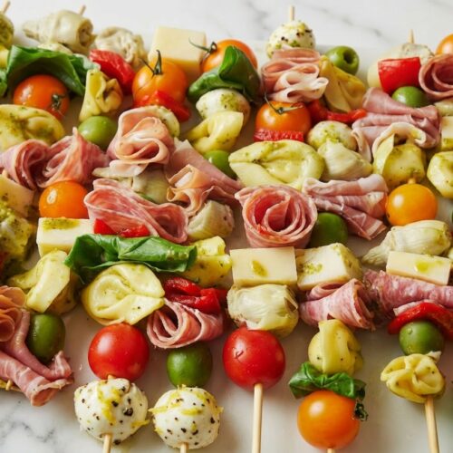 Antipasto skewers featuring mozzarella balls coated in a zesty lemon-peppercorn rub with cured meats and olives.