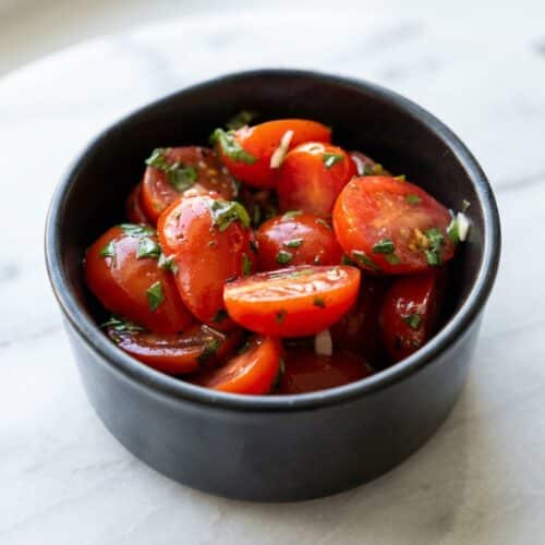 Marinated cherry tomatoes pricked whole for deep infusion with a savory umami-rich dressing in a bowl.