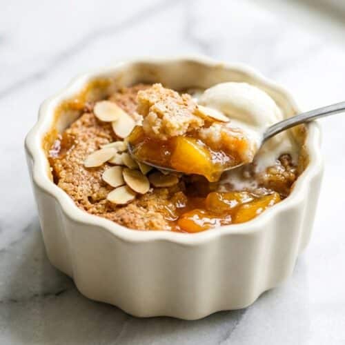 Golden mini peach cobbler in a ramekin with bourbon and almond infused yellow peaches.