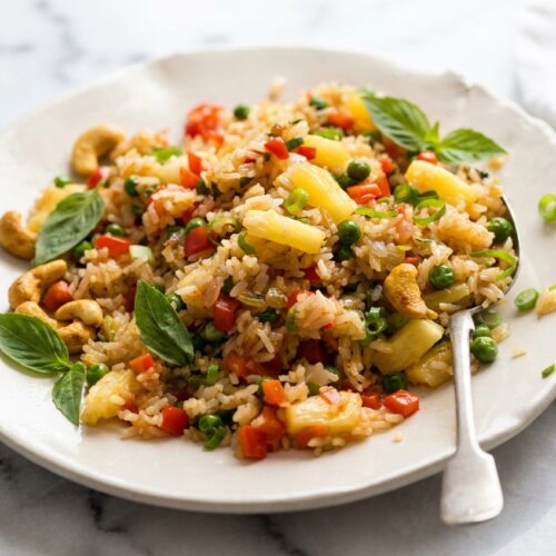Pineapple fried rice topped with curry-toasted salted cashews and fresh Thai basil in a pineapple boat.