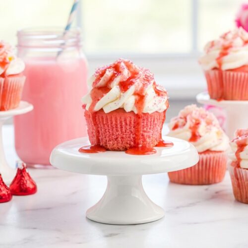 Pink velvet cupcakes topped with cream cheese frosting featuring a strawberry-infused buttermilk reduction.