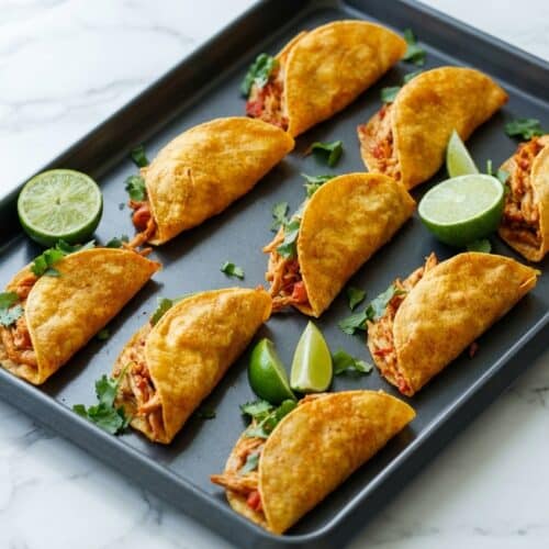 Crispy baked chicken tacos brushed with smoked paprika and garlic oil on a sheet pan.