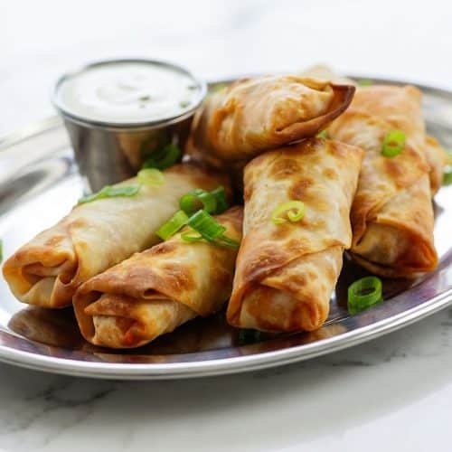 Crispy air fryer buffalo chicken egg rolls stacked on a plate, featuring a perfectly sealed wrapper and creamy emulsion.